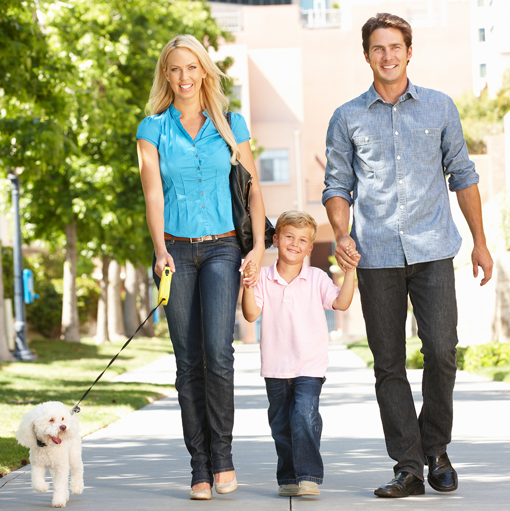 Father, mother, and son walk their dog along a sidewalk.